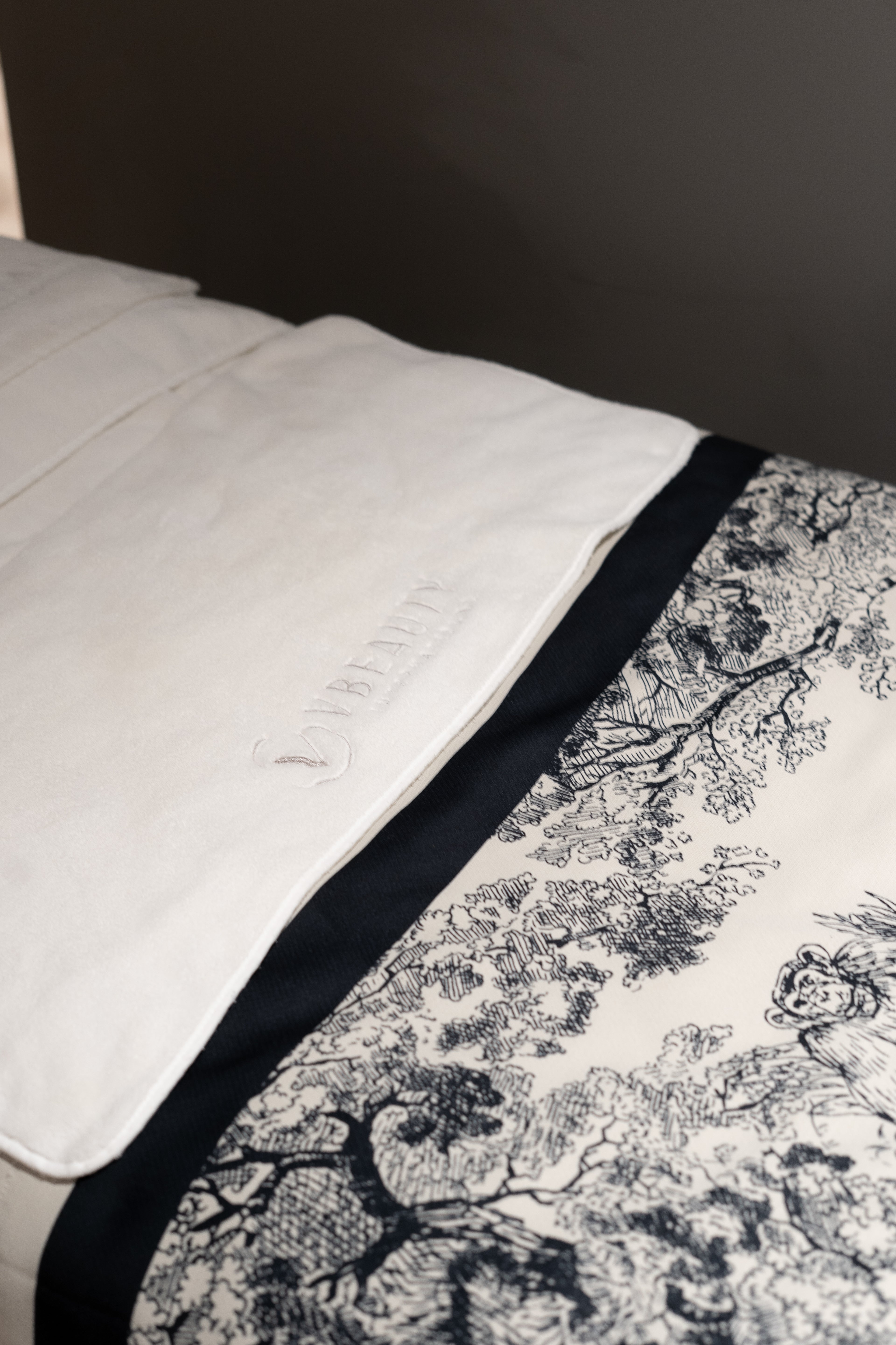 A close-up of a neatly made bed with white sheets and a black-and-white patterned blanket, set against a dark-colored wall.